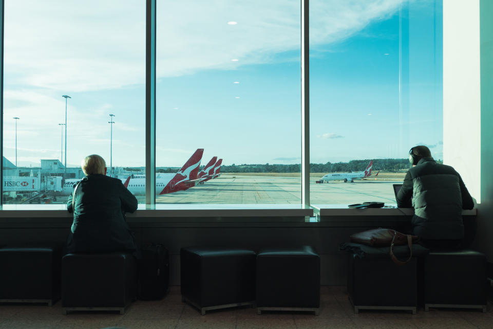 People waiting for departure in airport terminal with Qantas planes in view.