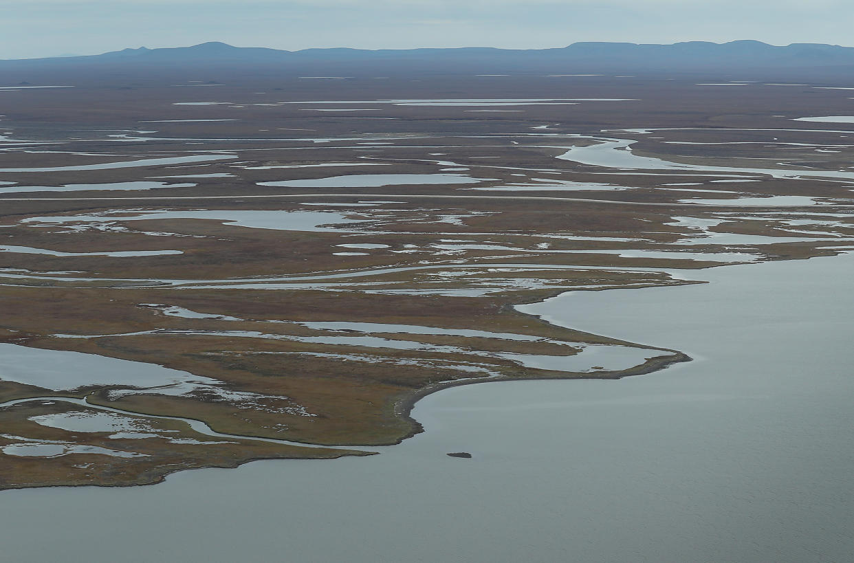 Aerial view of coastal land with larges swathes of water throughout with mountains in the background.