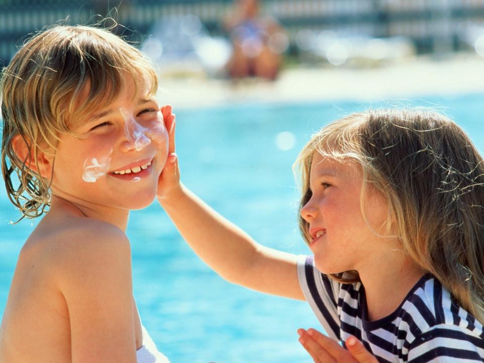 A girl puts sunscreen on another child's face.