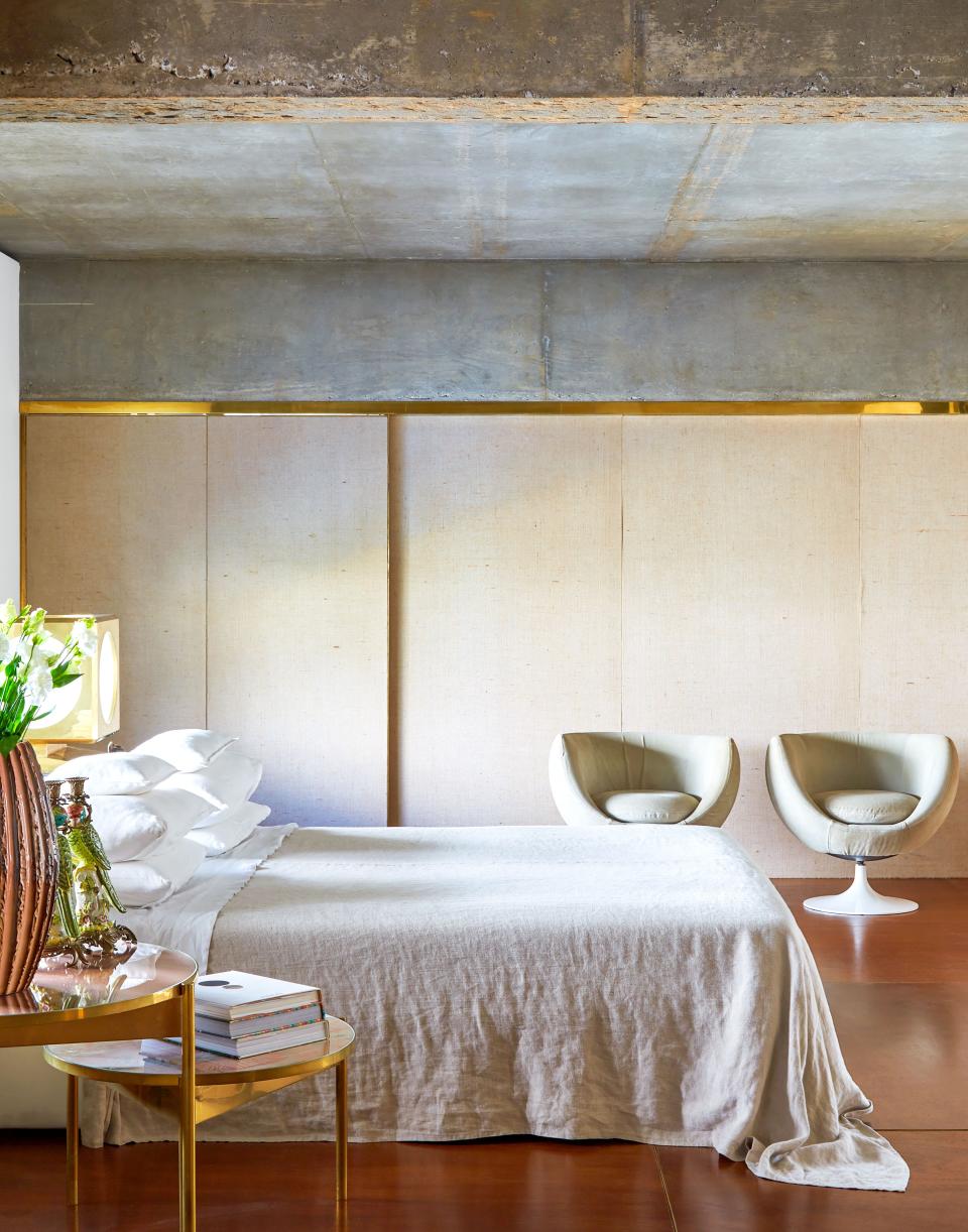 Closet doors covered in linen create a soft backdrop in the master bedroom. Custom bed; vintage armchairs; brass, fabric, and glass bedside tables.