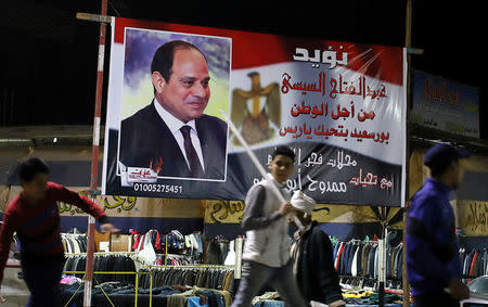 People walk in front of a banner supporting President Abdel Fattah al-Sisi's re-election hanging in a clothes market near the canal of Port Said, Egypt March 18, 2018. REUTERS/Mohamed Abd El Ghany