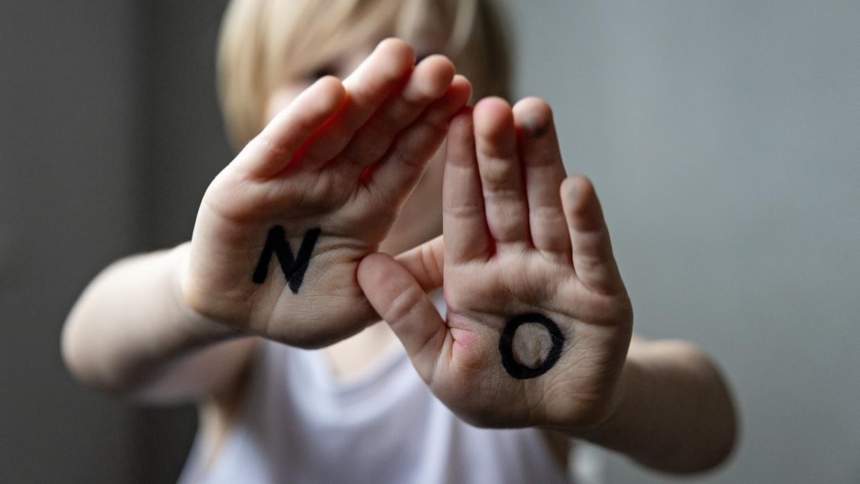  Kid with open hand palms showing word no written on them. 