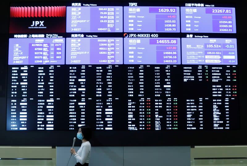 A TV reporter stands in front of a large screen showing stock prices at the Tokyo Stock Exchange after market opens in Toky