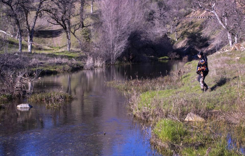 A woman stands beside a creek.