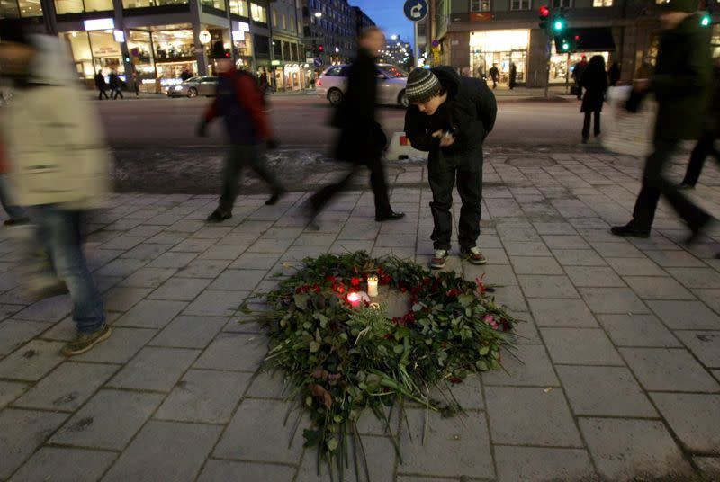 FILE PHOTO: A man bends over a bunch of roses and lit candles on a pavement in Stockholm