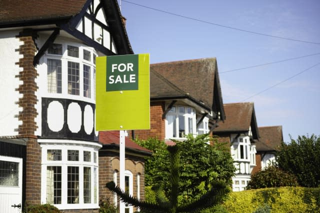 English suburban house with a 'For Sale' sign outside a row of houses, in the suburbs of a city, United Kingdom.