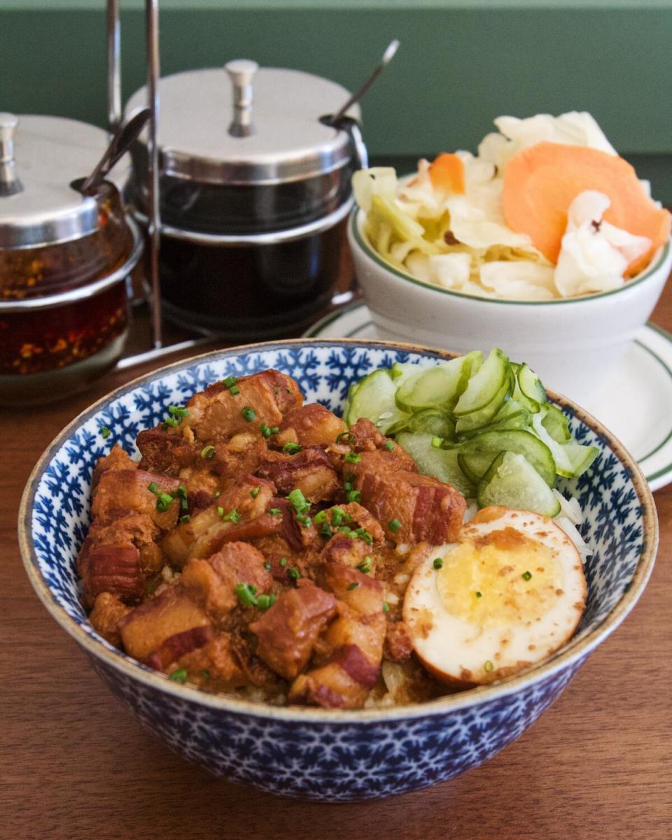 A bowl of braised pork belly with rice and egg from Liu's Cafe, with two jars of condiments and a bowl of pickled cabbage