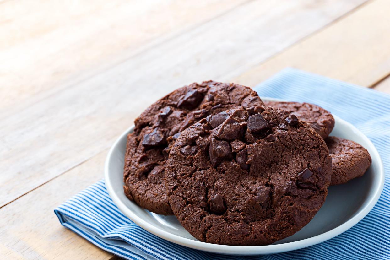 Four diabetic chocolate nut cookies on a white plate on a blue striped napkin with a wooden table background