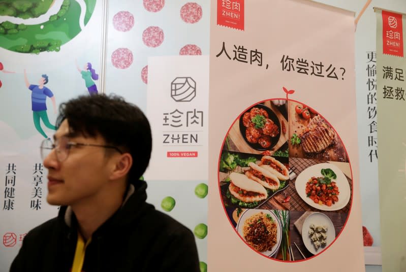 A man sits next to a poster at the booth of plant-based food company Zhenmeat at VeggieWorld fair in Beijing