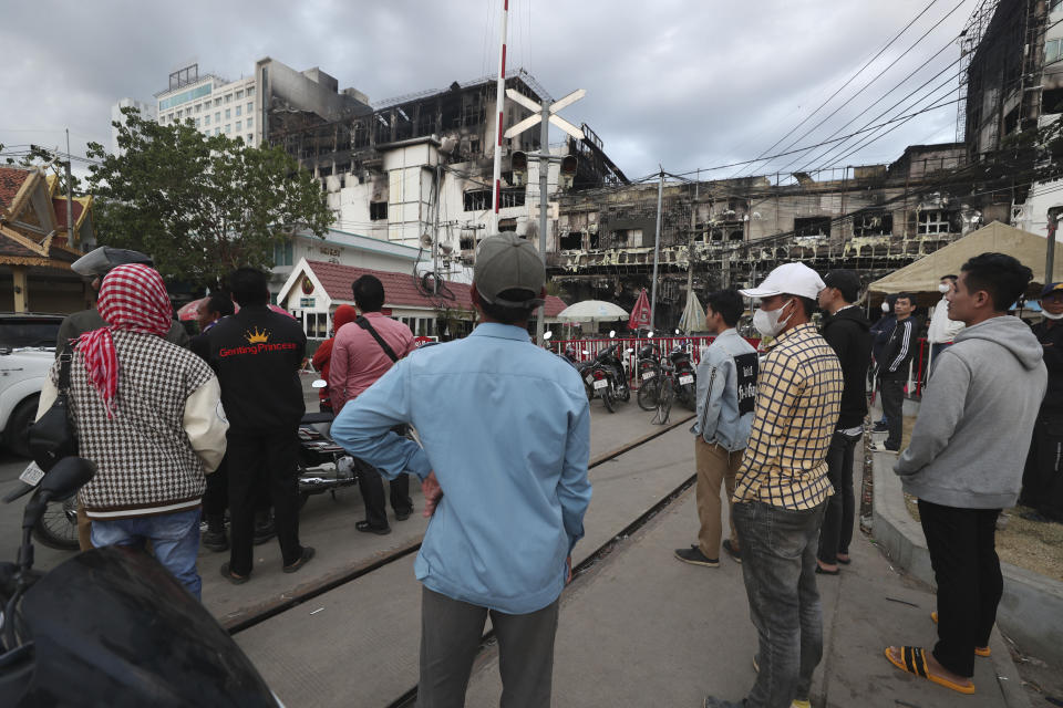 Residents gather near a ruined building at the scene of a massive fire at a Cambodian hotel casino in Poipet, west of Phnom Penh, Cambodia, Friday, Dec. 30, 2022. The fire at the Grand Diamond City casino and hotel Thursday injured over 60 people and killed more than a dozen, a number that officials warned would rise after the search for bodies resumes Friday. (AP Photo/Heng Sinith)