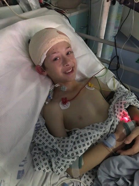 Ben Parton lays in a hospital bed while hooked to a machine and a bandage around his head.