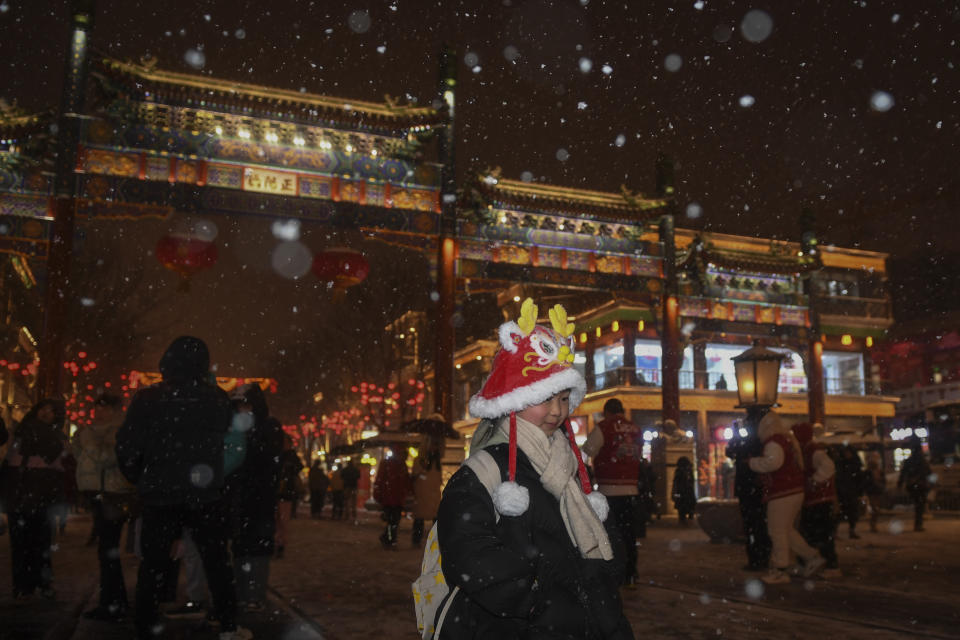 In this photo released by Xinhua News Agency, a child wearing a dragon headgear and other visitors tour the Qianmen shopping street during a snowfall in Beijing on Tuesday, Feb. 20, 2024. Heavy snow has blanketed northern and central China, disrupting traffic and forcing schools to cancel classes. (Ju Huanzong/Xinhua via AP)