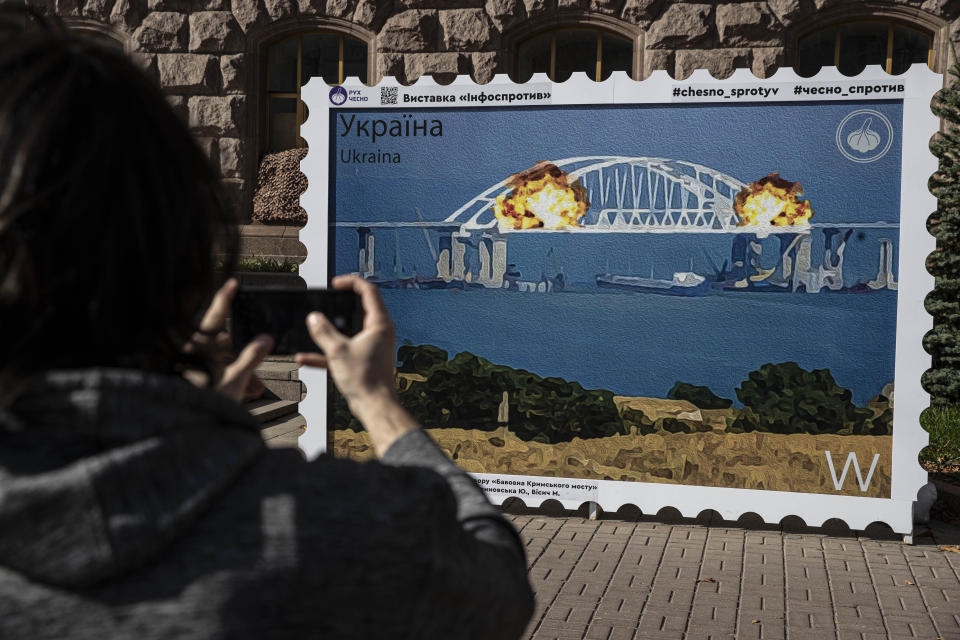 People take photos Wednesday in Kyiv, Ukraine, in front of an image of a stamp showing explosions on the Kerch Strait Bridge. 