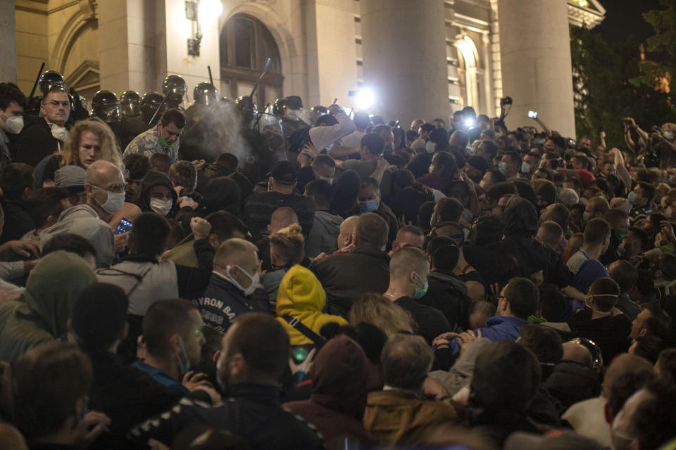 Police officers use pepper spray on demonstrators in front of the Serbian parliament in Belgrade, Serbia, Tuesday, July 7, 2020. Thousands of people protested the Serbian president's announcement that a lockdown will be reintroduced after the Balkan country reported its highest single-day death toll from the coronavirus Tuesday. (AP Photo/Marko Drobnjakovic)