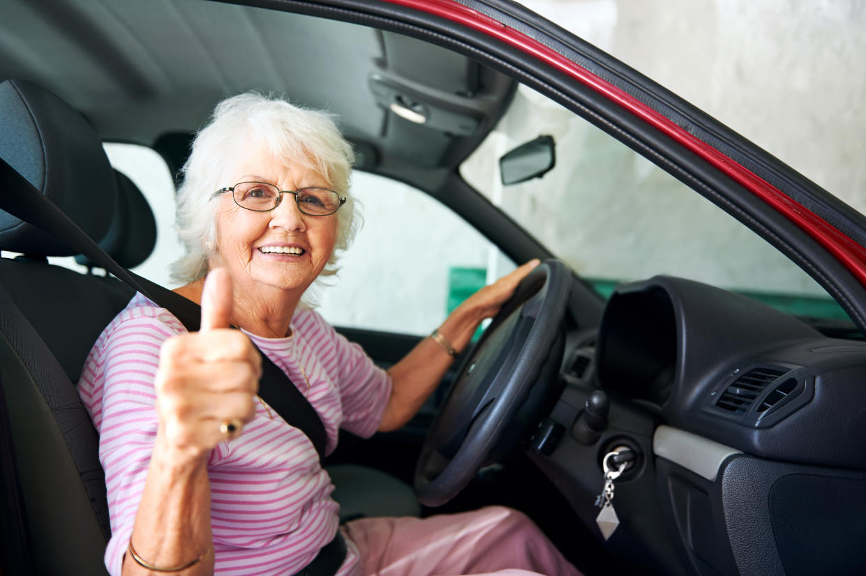 An positive older woman sitting in a car showing a thumbs up