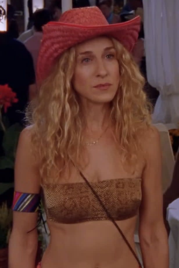 Sarah Jessica Parker wearing a strapless top, cowboy hat, and colorful armband at an outdoor event with people in the background