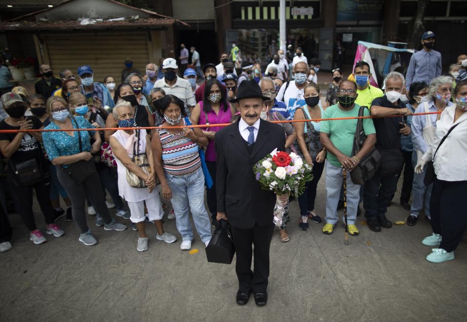 Augusto Santos, vestido como el difunto Dr. José Gregorio Hernández, está de pie junto a los devotos del médico frente a la iglesia La Candelaria, donde está enterrado en Caracas, Venezuela, el lunes 26 de octubre de 2020. (AP Foto/Ariana Cubillos)