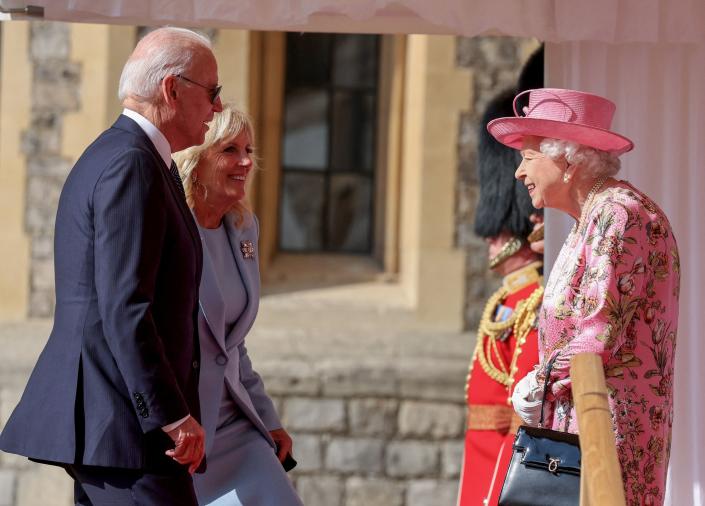 Queen Elizabeth II, with the Queen's Guards in bearskin hats in the background, greets President Joe Biden and first lady Jill Biden.