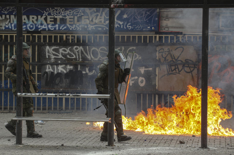 A petrol bomb explodes near a police officer during clashes with anti-government protesters in Santiago, Chile, Monday, Nov. 18, 2019. According to the Medical College of Chile at least 230 people have lost sight after being shot in an eye in the last month while participating in the demonstrations over inequality and better social services. (AP Photo/Esteban Felix)