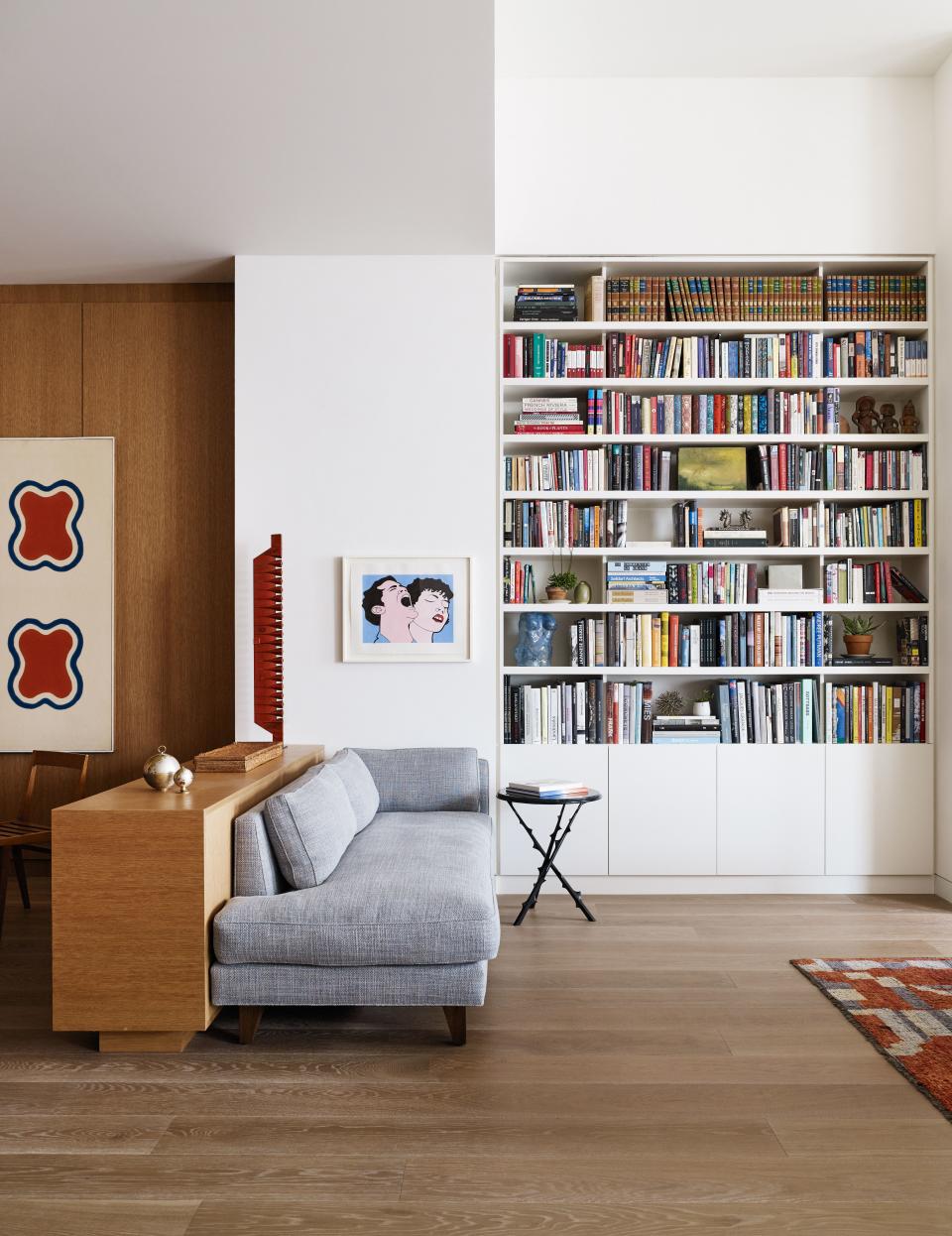 Santos created a small reading nook to act both as a place to take advantage of the gorgeous book shelves and as a transition to the open plan in the front of loft. The custom chaise, made to delineate the space, is by Laura Santos Interiors and fabricated by Dune. The petite and decorative side table by Hervé Van der Straeten from Maison Gerard. The painting is by John Wesley.