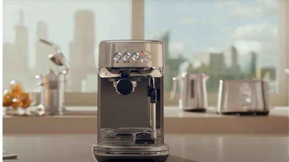 Breville's bambino plus espresso machine on a countertop with a window looking over the city in the background
