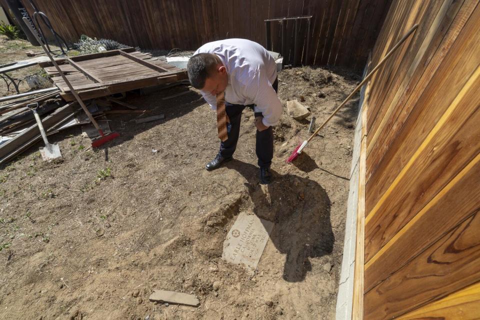 A man bends over to read an uncovered headstone in the backyard of a house in Lawndale.