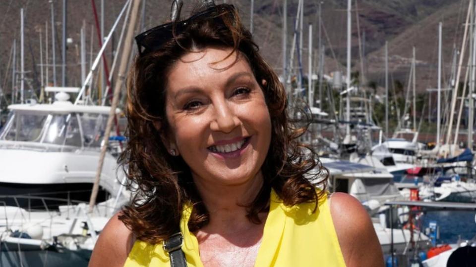 Jane McDonald in a yellow outfit in front of several boats