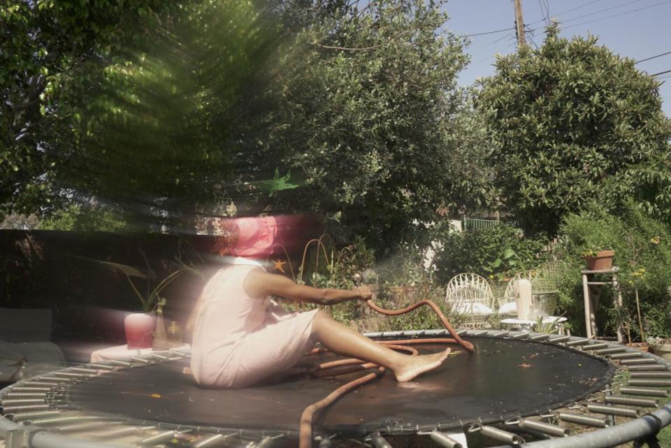 A woman sits on a trampoline with a hose.