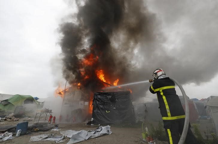 Répétiton titre Un pompier éteint un feu à la "jungle" de Calais. Seul un millier de migrants sur plus de 6.000 étaient encore présents mercredi matin dans le campement de Calais. /Photo prise le 26 octobre 2016/REUTERS/Philippe Wojazer