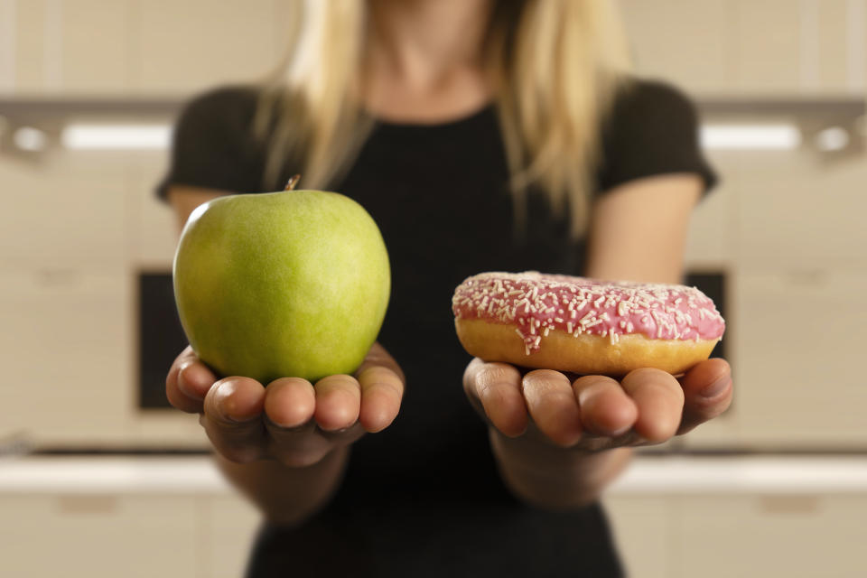 Woman holding an apple and donut. Source: Getty Images