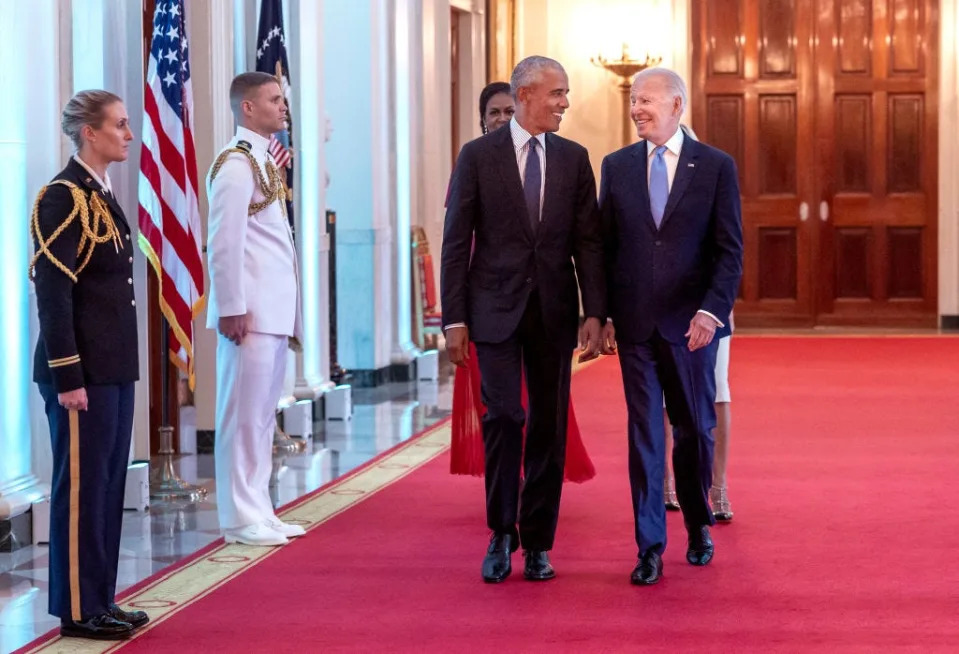 Barack Obama and Joe Biden walk down a hall in the White House.