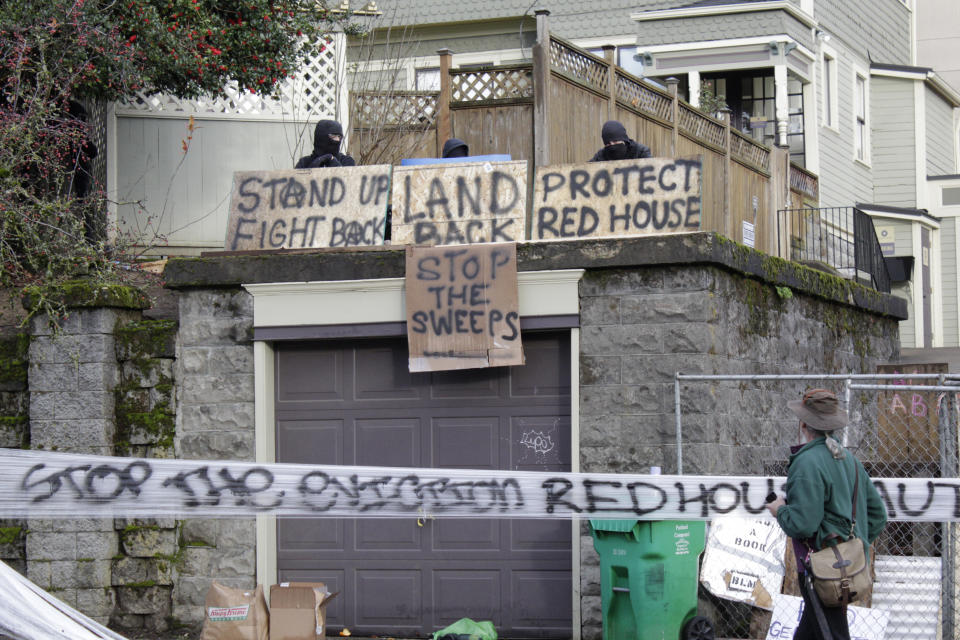 Masked protesters by an occupied home speak with a neighborhood resident opposed to their encampment and demonstration in Portland, Ore., on Wednesday, Dec. 9, 2020. Makeshift barricades erected by protesters are still up in Oregon's largest city a day after Portland police arrested about a dozen people in a clash over gentrification and the eviction of a family from a home. (AP Photo/Gillian Flaccus)