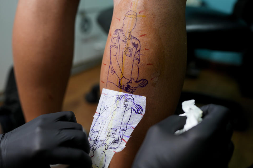 El artista Mariano Finkelstein trabaja en un tatuaje del arquero argentino Emiliano Martínez haciendo un gesto con su trofeo de guante de oro durante la ceremonia de premiación de la Copa del Mundo en Qatar 2022, en el cliente Valentin Bobadilla en Buenos Aires, Argentina, el jueves 29 de diciembre de 2022. (AP Foto/Natacha Pisarenko)