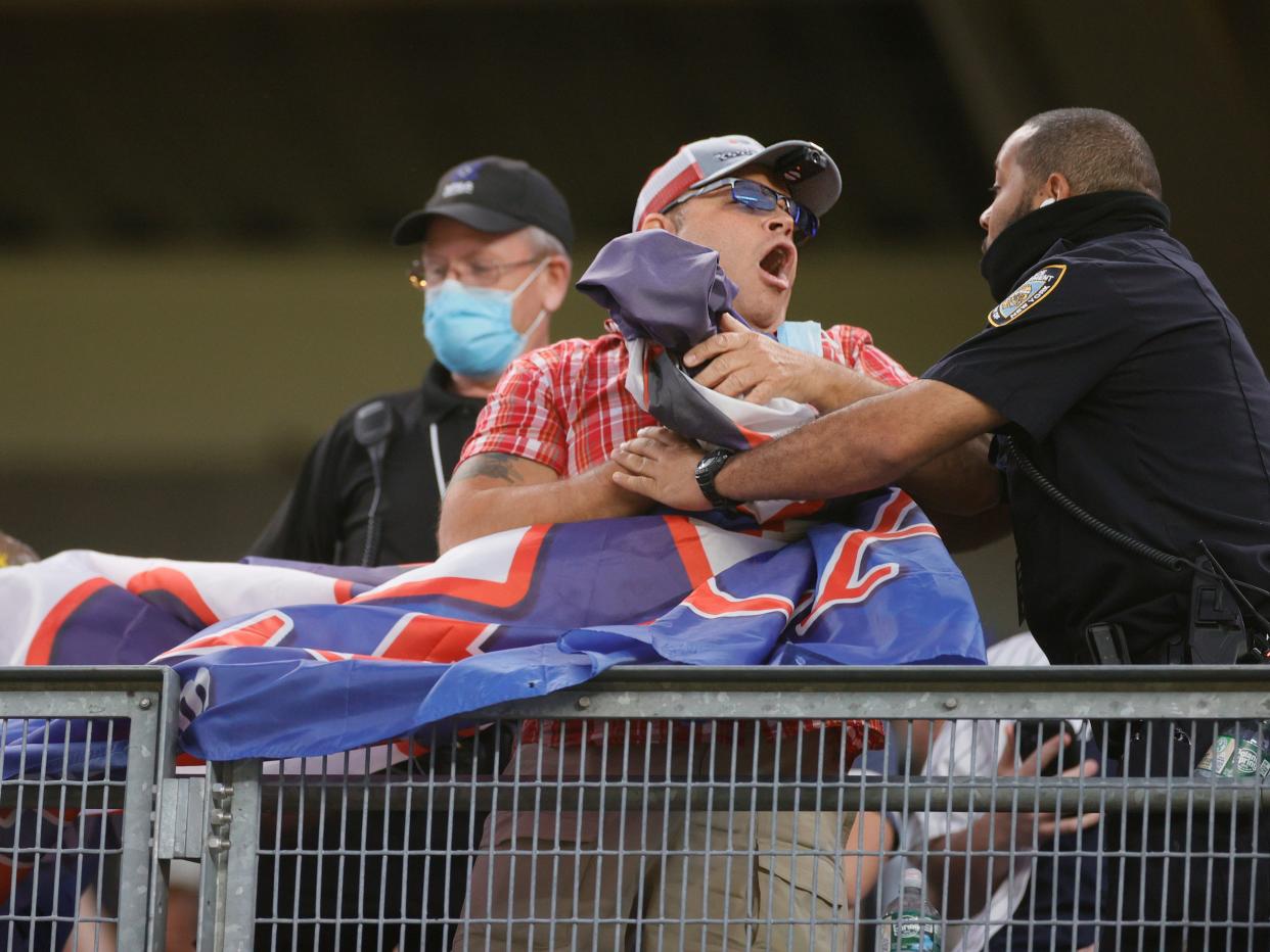 A security guard grabs a man gathering a large blue and red flag in his arms.