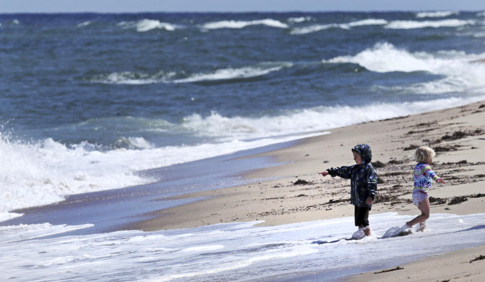In this May 22, 2019, photo, two children play in the surf at Newcomb Hollow Beach, where a boogie boarder was bitten by a shark and later died of his injuries the previous summer, in Wellfleet, Mass. Cape Cod beaches open this holiday weekend, just months after two shark attacks, one of which was fatal, rattled tourists, locals and officials. Some precautionary new measures, such as emergency call boxes, have yet to be installed along beaches where great whites are known to frequent. (AP Photo/Charles Krupa)