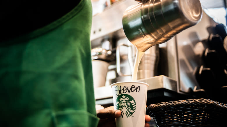 Starbucks barista pouring milk into coffee