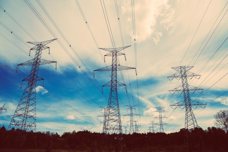 Layers of high tension electrical pylons and power lines against blue sky with clouds