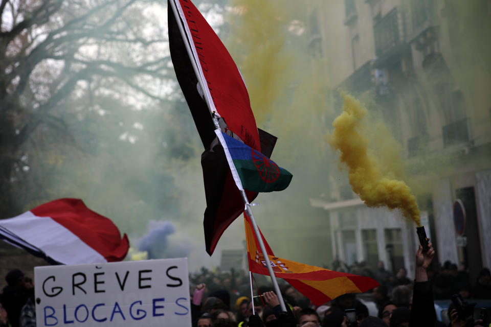 A sign reading "Strikes Blockades", flags with flares are displayed during the yellow vests 56th round demonstration in Paris, Saturday, Dec. 7, 2019. A few thousand yellow vest protesters marched Saturday from the Finance Ministry building on the Seine River through southeast Paris, pushing their year-old demands for economic justice and adding the retirement reform to their list of grievances. (AP Photo/Francois Mori)