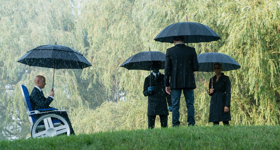 Four people dressed in black holding umbrellas in the rain