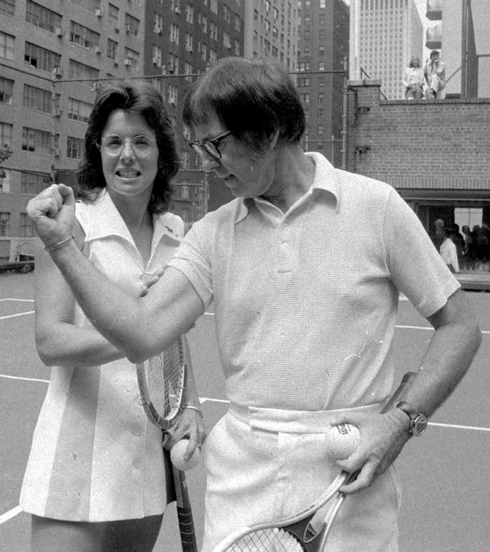 Billie Jean King checks on the flexing prowess of her "Battle of the Sexes" nemesis Bobby Riggs on a tennis court.