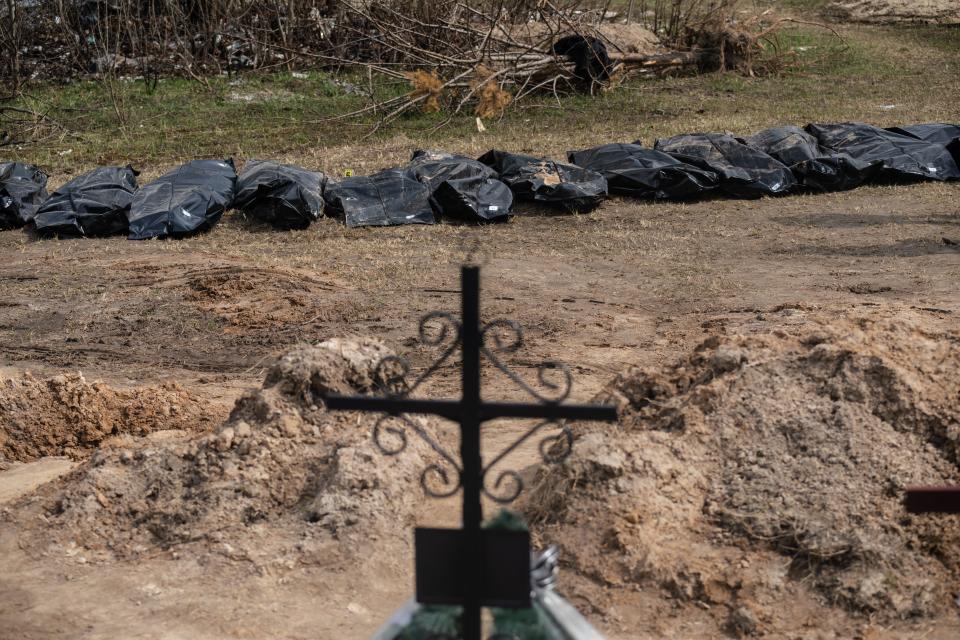 Bags of bodies are seen in the background, as a cross appears in the foreground.