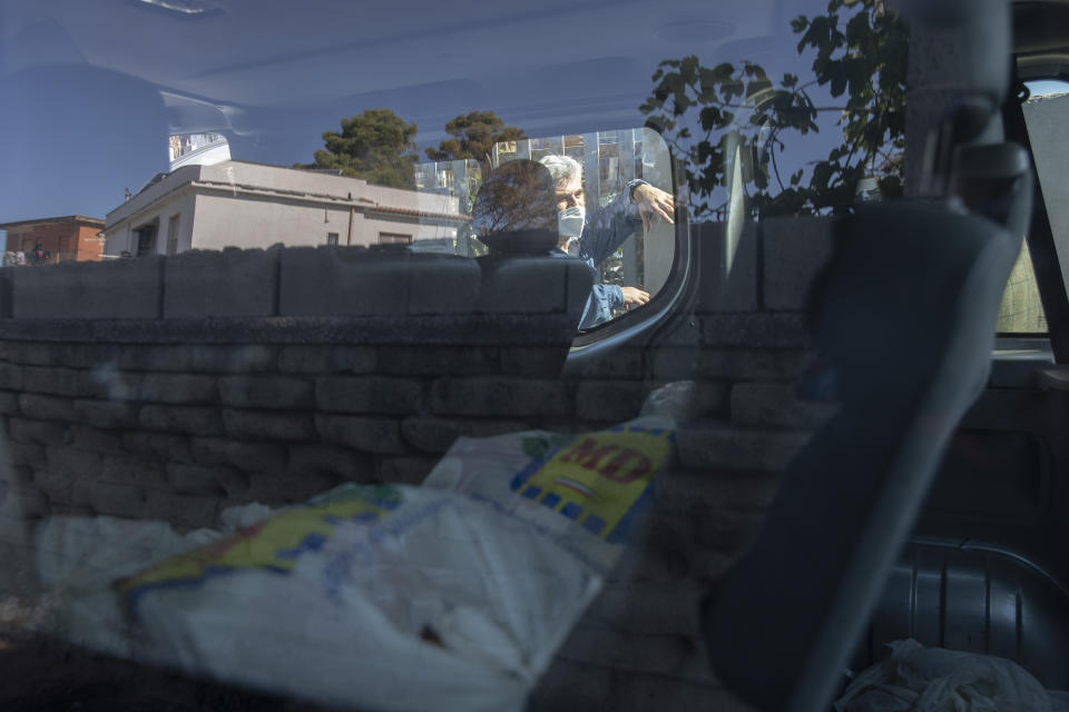 In this photo taken on Monday, April 27, 2020, father Daniele Moschetti is seen trough a window of his van full of shopping bags as he brings food to the people of Castel Volturno, near Naples, Southern Italy. Father Daniele Moschetti spent a decade doing missionary work in the slums of Nairobi and now he finds his work to be similar in his own country.They are known as “the invisibles,” the undocumented African migrants who, even before the coronavirus outbreak plunged Italy into crisis, barely scraped by as day laborers, prostitutes and seasonal farm hands. Locked down for two months in their overcrowded apartments, their hand-to-mouth existence has grown even more precarious with no work, no food and no hope. (AP Photo/Alessandra Tarantino)