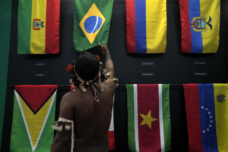 FILE - An indigenous man passes his hand over the Brazilian flag in a flag pavilion of the States parties to the Amazon Cooperation Treaty, during the Amazon Dialogue meetings at the Hangar convention center in Belem, Brazil, Aug. 6, 2023. The two-day Amazon Summit opens Aug. 8, 2023, in Belem, where Brazil hosts policymakers and others to discuss how to tackle the immense challenges of protecting the Amazon and stemming the worst of climate change. (AP Photo/Eraldo Peres, File)