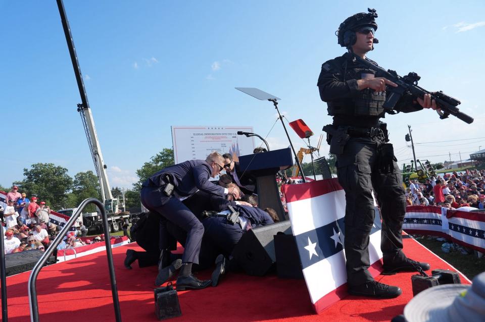 Secret Service agents converge on Trump on the stage of his Pennsylvania campaign rally, while a uniformed agent stands nearby holding a rifle.