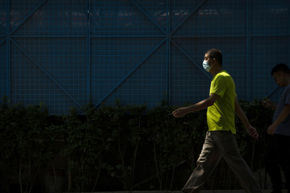 A man wearing a face mask walks along a path in a public park in Beijing, Tuesday, Aug. 30, 2022. (AP Photo/Mark Schiefelbein)