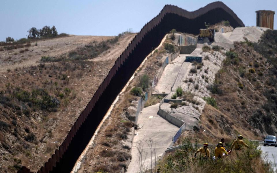 Firefighters carry the body of an alleged smuggler murdered near the US-Mexico border wall in Tijuana on June 15 - Guillermo Arias/AFP