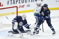 Winnipeg Jets goaltender Connor Hellebuyck (37) stops a shot shot as teammate Brenden Dillon (5) defends against Vancouver Canucks' Brock Boeser (6) during second-period NHL hockey game action in Winnipeg, Manitoba, Thursday, Jan. 27, 2022. (John Woods/The Canadian Press via AP)