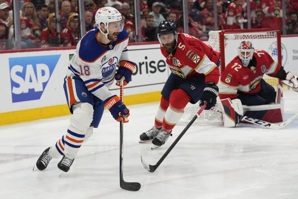 Edmonton Oilers left wing Zach Hyman (18) looks to pass the puck as Florida Panthers defenseman Aaron Ekblad (5) defends during the third period of Game 2 of the NHL hockey Stanley Cup Finals, Monday, June 10, 2024, in Sunrise, Fla. (AP Photo/Wilfredo Lee)