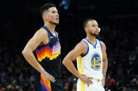 Phoenix Suns guard Devin Booker and Golden State Warriors guard Stephen Curry (30) watch a free throw during the first half of an NBA basketball game, Tuesday, Nov. 30, 2021, in Phoenix. (AP Photo/Matt York)