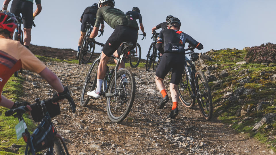 Gravel riders riding and walking up a gravel track